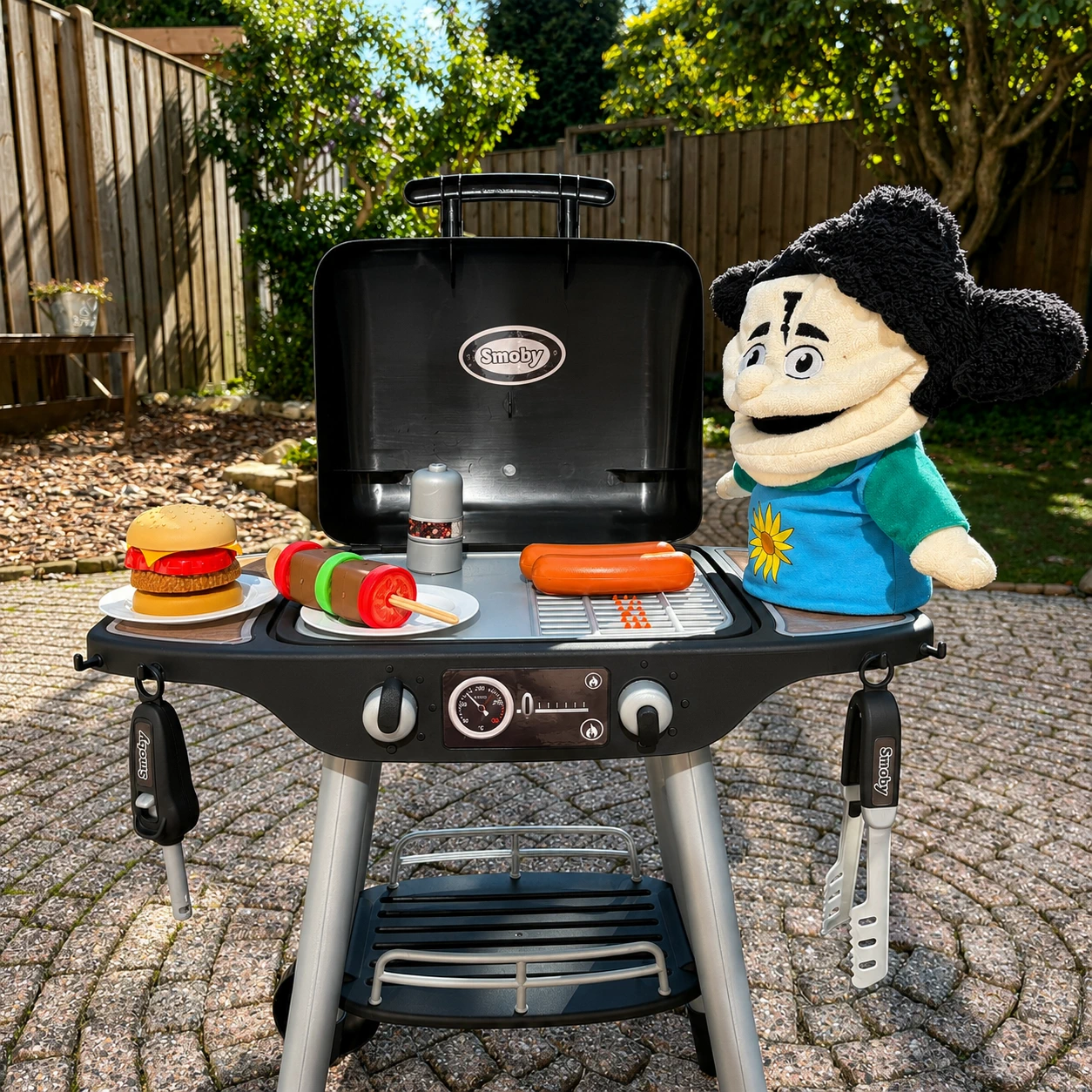 Foto in de tuin van de speelgoed barbecue met de handpoppen van de methode.