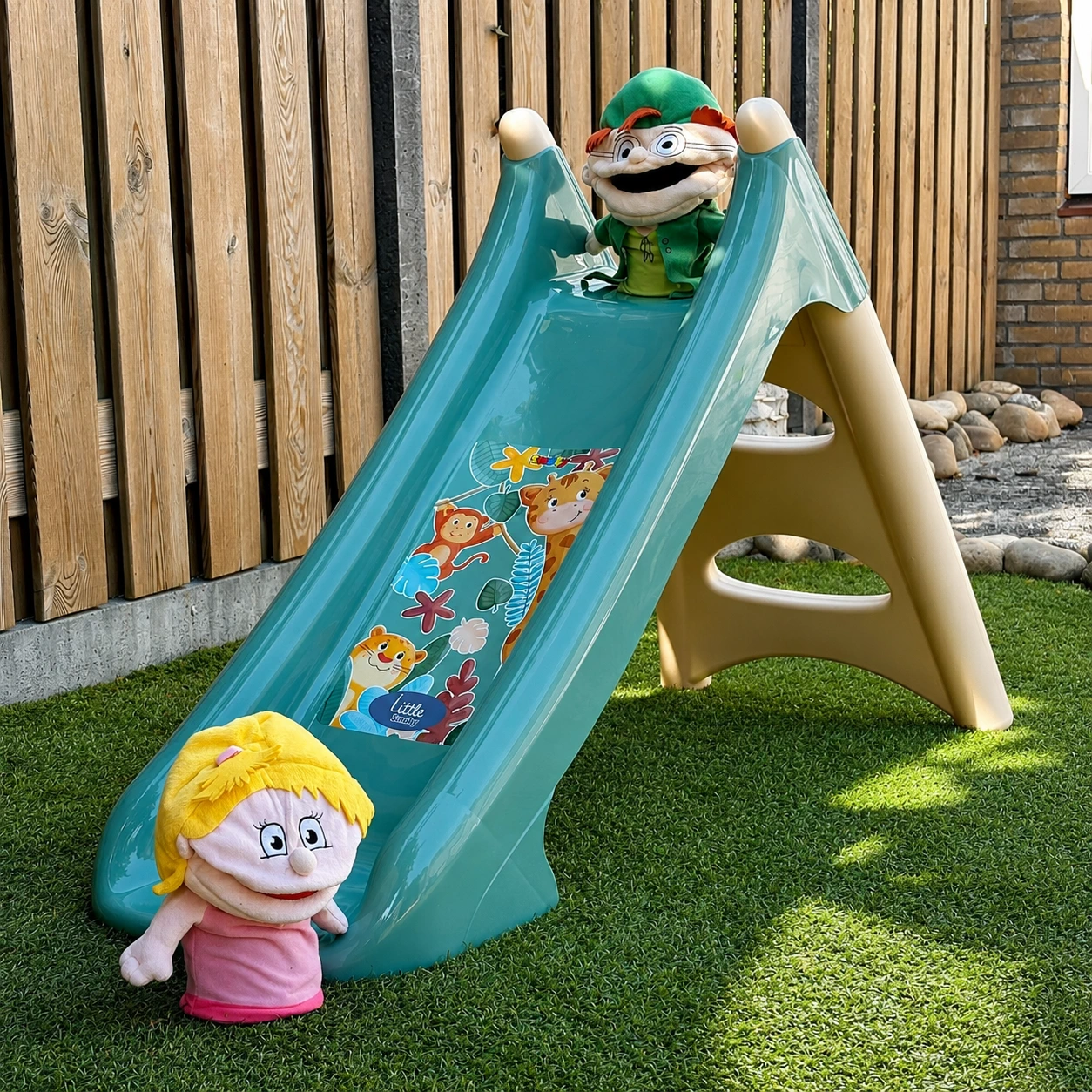 Foto in de tuin van de glijbaan met de handpoppen van de methode.